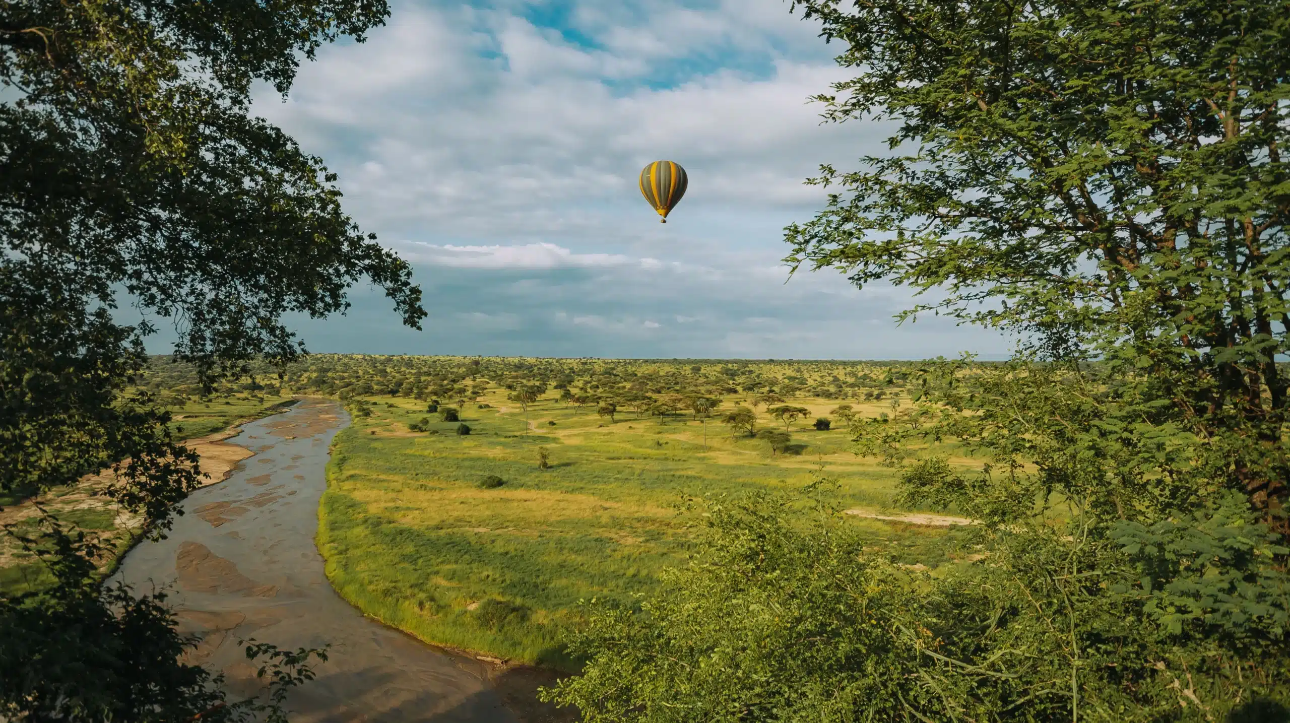Hot air balloon over green plains and a river