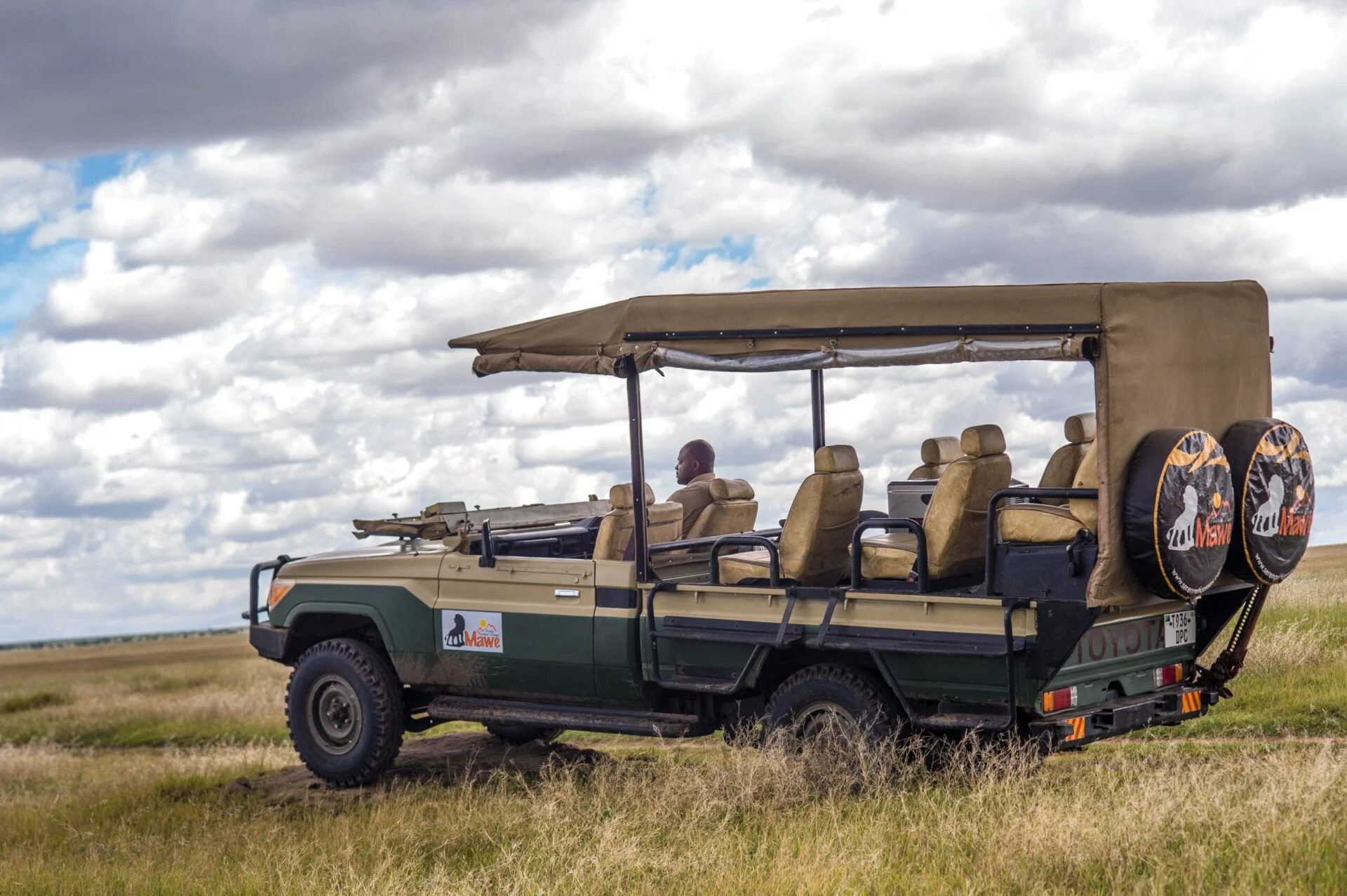 An open-sided Mawe Lodges safari vehicle parked out on the grass plains