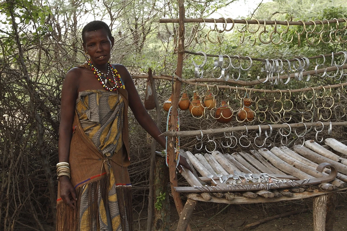 A Datoga woman beside a stall of handmade jewellery and blades