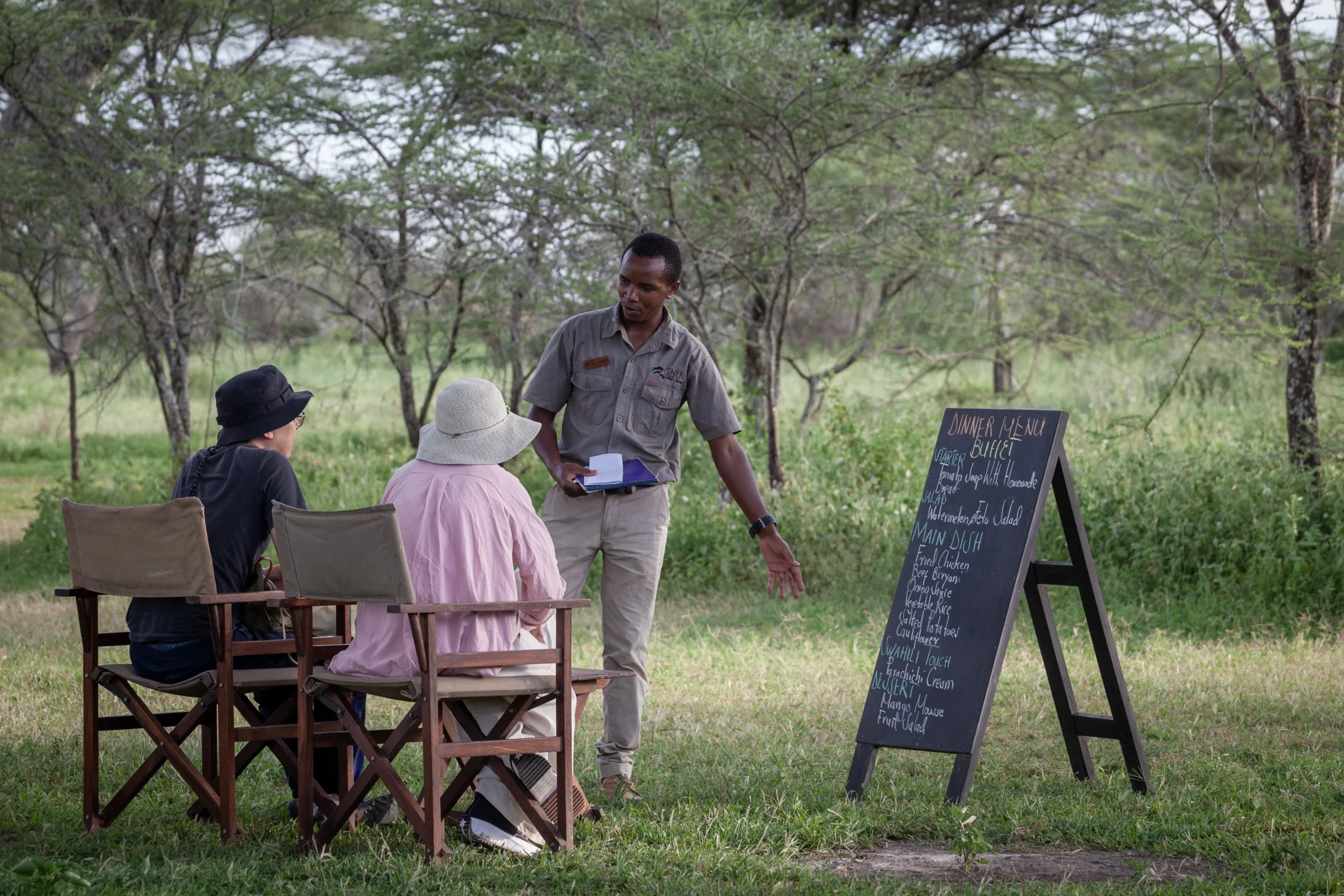 A camp host talking guests through the dinner menu board on the grass