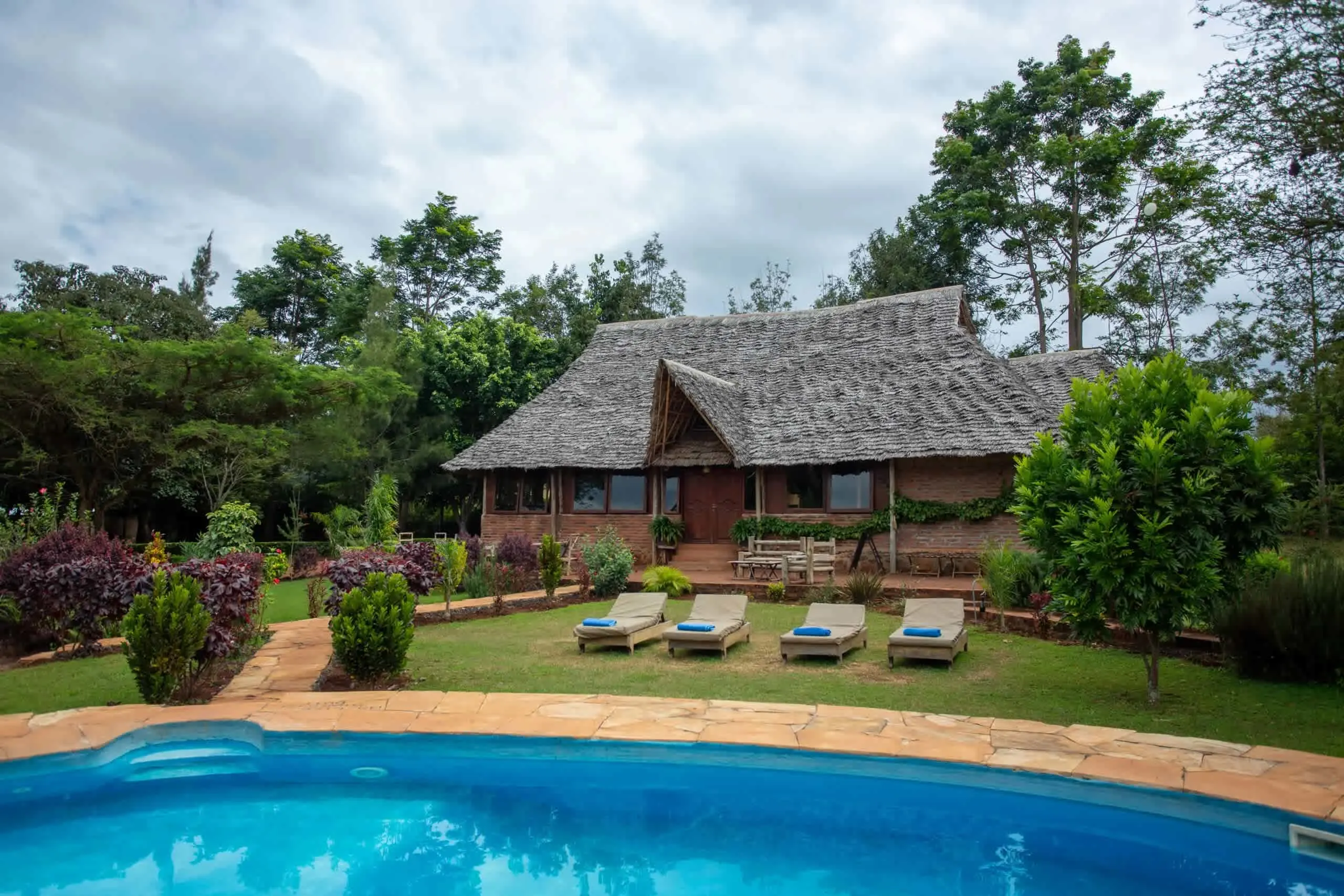 A picturesque house featuring a thatched roof and pool, situated in the Karatu Tented Lodge, Ngorongoro Highlands.