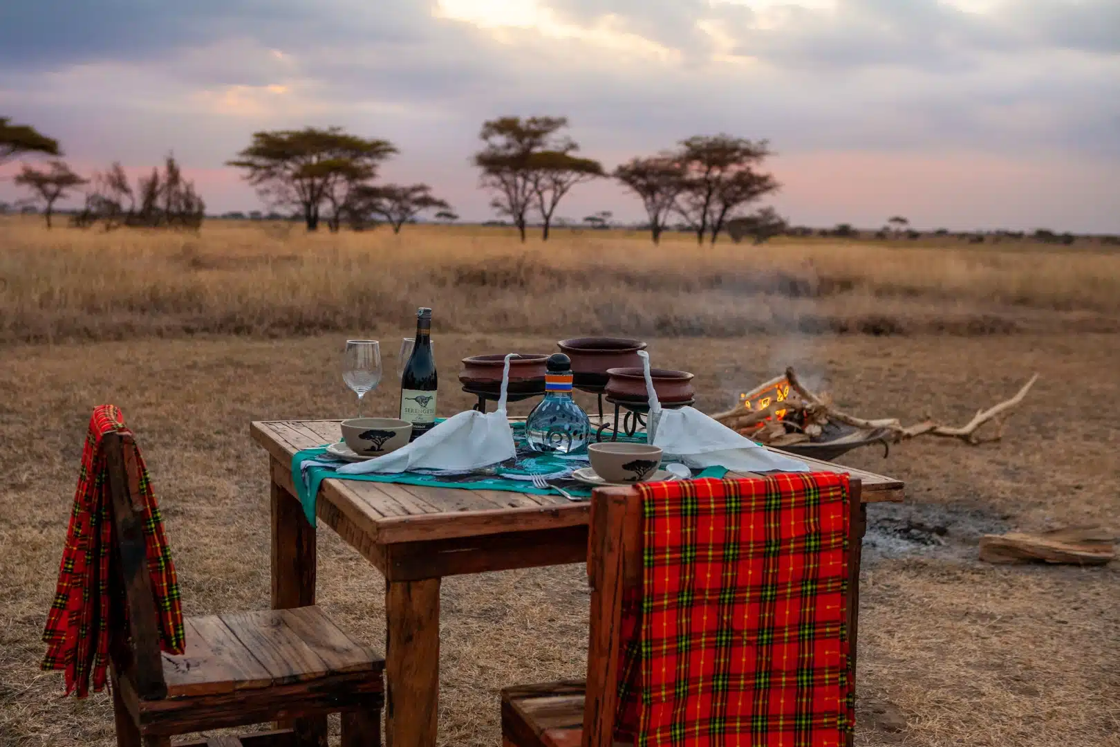 A dinner table set beside the campfire at dusk on the plains
